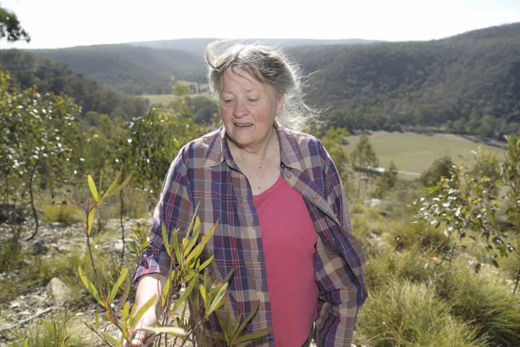 Charlotte Stahl, habitat conservationist smiles and looks down at a plant in an open area.