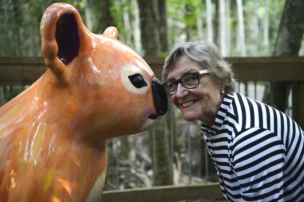 Margret Meagher smiles next to one of the koala sculptures on the Hello Koalas Sculpture Trail